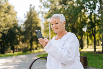 Portrait of elegant gray-haired senior lady holding using mobile phone, smiling looking to screen,...