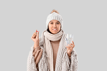 Sick young woman with pill on grey background