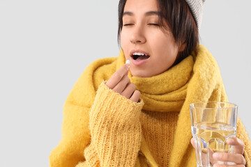 Sick young woman taking pill on grey background