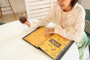 Pretty young woman reading menu while drinking wine in cafe