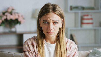 Young woman feeling down and crying at home, experiencing sadness, grief, or depression, with tears...
