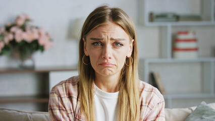 Sad woman is crying on the sofa at home, feeling depressed and lonely, she is suffering from grief...