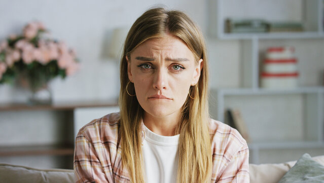 Portrait of a young woman sitting on a sofa in her living room, expressing deep sadness and vulnerability, with tears streaming down her face, reflecting feelings of loneliness and despair