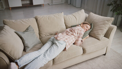 Young woman lies sleeping peacefully on a comfortable sofa in her living room, enjoying a moment of...