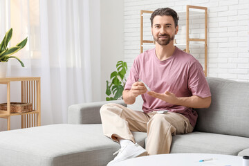 Diabetic young man using lancet pen on sofa at home