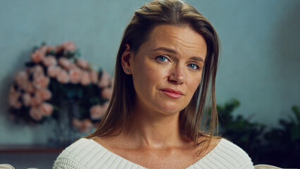 Portrait of a sad, lonely woman sitting on a sofa in her living room, expressing melancholy and...