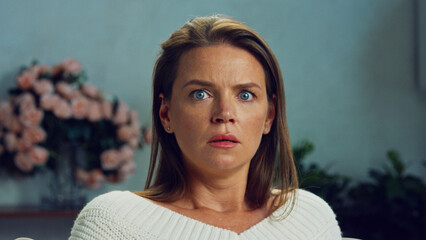 Portrait of a scared woman showing fear in her eyes while sitting on a sofa in her living room, a...