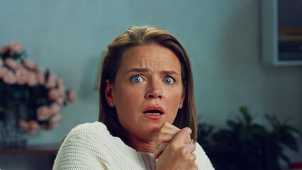 Woman sitting on the sofa in her living room, watching a horror movie and feeling intense fear....