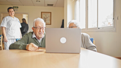 Elderly couple learns to use a laptop with a nurse standing by.