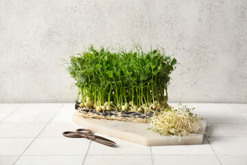 Board with fresh micro green sprouts and scissors on light tile table