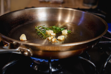 Garlic and rosemary in oil in a skillet on a gas stove 