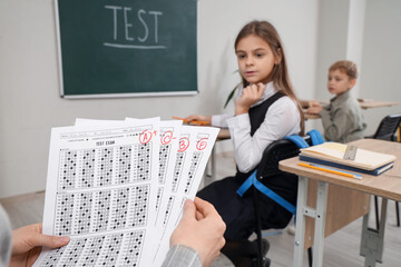 Fototapeta premium Teacher with checked answer sheets in classroom, closeup