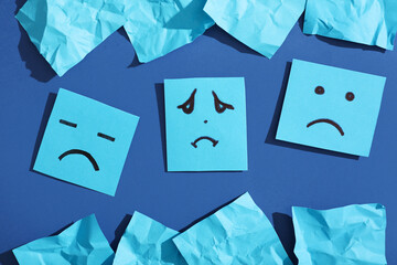 Paper sheets with drawn sad faces on blue background