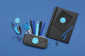 Office stationery with drawn sad faces on blue background