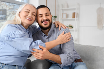 Young man with his mother hugging on sofa at home