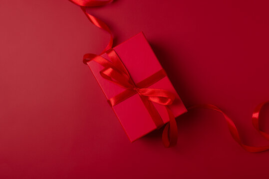 Xmas gift box and decoration celebration in Christmas theme. Red present box on red background. Valentines day gift box with red ribbon. Monochrome color scheme, top view