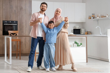 Happy Muslim family holding hands in kitchen