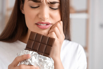 Young woman suffering from toothache with chocolate bar at home, closeup