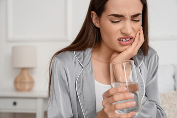 Young woman in pajamas with glass of water suffering from toothache at home, closeup