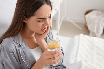 Young woman in pajamas with lemon water suffering from toothache at home, closeup