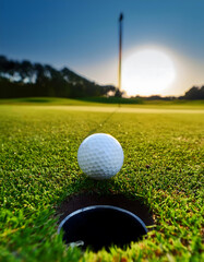 A white golf ball placed next to the hole on a green on a golf course.