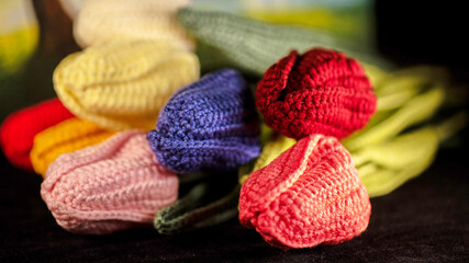 A bunch of colorful, knitted tulips displayed against a black background, each bloom showcasing vibrant hues of pink, yellow, purple, and red for decorative appeal.
