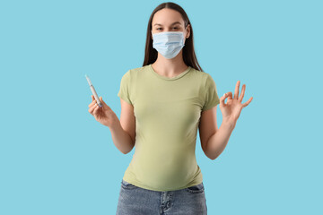 Young pregnant woman in medical mask with gestational diabetes and lancet pen showing OK on blue...