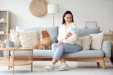 Young woman with fluffy dog and lint roller at home