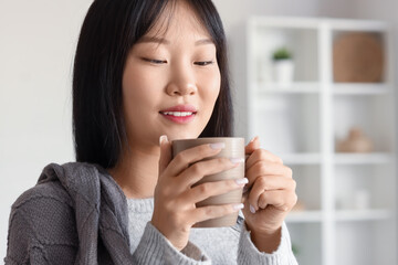 Young Asian woman with grey plaid and cup of tea at home, closeup