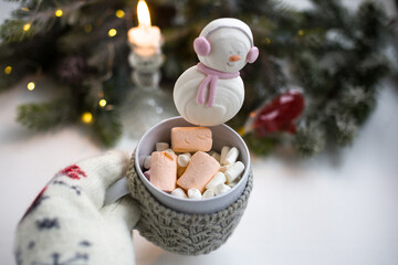 Women's woolen mittens with a mug of hot drink and marshmallows. Winter