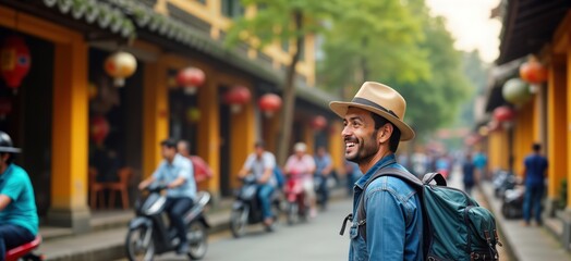 Obraz premium Happy solo traveler enjoys sightseeing in Hoi Ancient town Vietnam. Man with backpack, hat walks along street. Colorful buildings, lanterns line street. Many people around street. Vacationing in