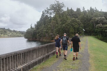 Obraz premium Family hike along a dam wall path, enjoying the scenery. Cloudy day. Waitakere Dam, Waitakere Ranges, Auckland, New Zealand
