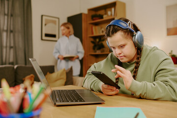 Caucasian girl with Down syndrome wearing sitting at desk in front of laptop in living room at...