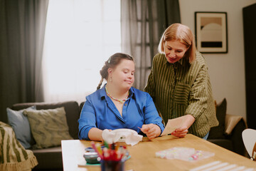 Mature Caucasian woman and her daughter with Down syndrome looking at embroidery pattern image and...
