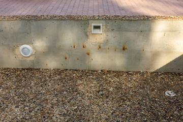 A wall with a vent on it and a white box on the wall, elements of an artificial pond or fountain