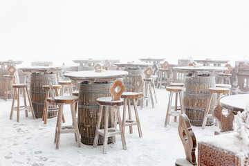 Snow-covered outdoor patio with wooden barrels and chairs in winter wonderland