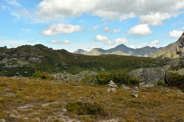 Ritual stone pyramids on a flat meadow in front of a high mountain range on a sunny summer day.