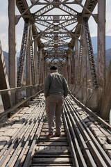 Fototapeta premium Rear view of a man walking across a railway bridge. Concept: enjoyment of free time traveling. Composition with copy space using symmetry and central perspective to generate harmony.