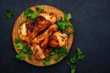 Baked chicken legs or drumsticks in spices on wooden serving board, black background, top view