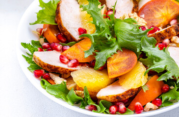 Winter persimmon salad with grilled chicken, pomegranate, walnuts, oranges and lettuce, white background, top view