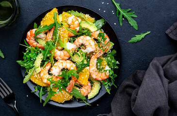 Yummy shrimp salad with avocado, orange, arugula and sesame seeds on black table background. Top...