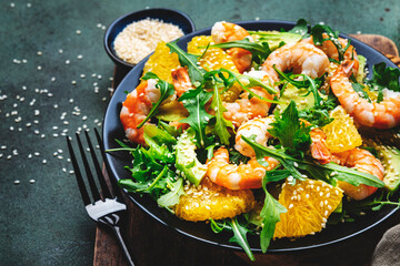 Delicious shrimp salad with avocado, orange, arugula and sesame seeds on green table background. Top view