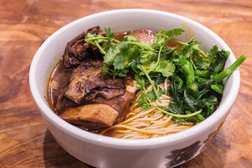 A bowl of braised beef noodle soup on a wooden table