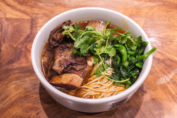 A bowl of braised beef noodle soup on a wooden table