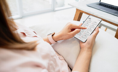 Businesswoman using smartphone with monthly calendar to plan 2025 activities. Scheduling and...