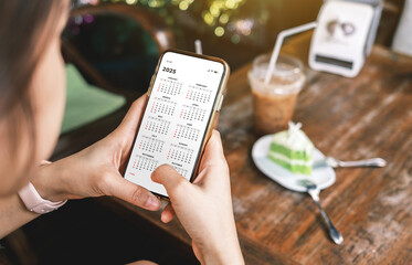 Businesswoman using smartphone with monthly calendar to plan 2025 activities. Scheduling and...