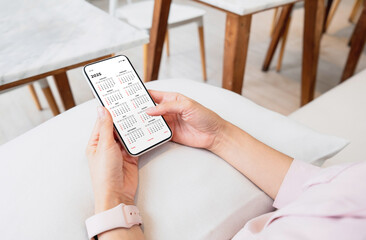 Businesswoman using smartphone with monthly calendar to plan 2025 activities. Scheduling and...