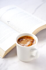 テーブルの上の開いたペーパーバック（洋書）と、コーヒーの入ったコーヒーカップで、コーヒーを飲みながらゆっくりと読書を楽しんでいるイメージ
