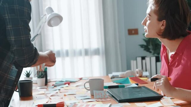 Top view of smart designer holding color palette while project manager looking at design and choosing color for program. Professional businesswoman taking a note while design creative logo. Symposium.