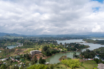 Fototapeta premium Serene lake nestled in a valley, surrounded by lush greenery and rolling hills under a cloudy sky.